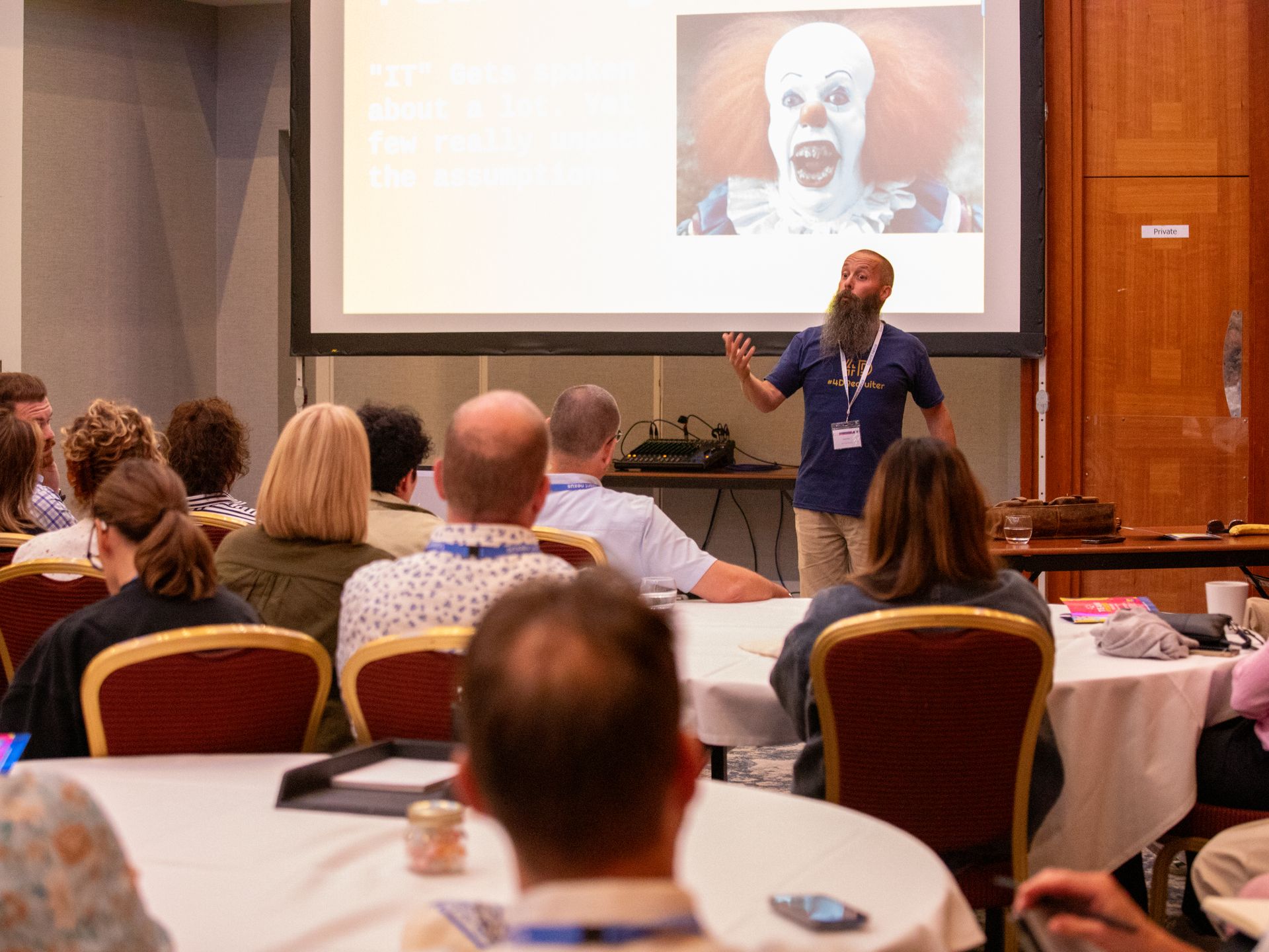 A man is giving a presentation to a group of people sitting at tables.