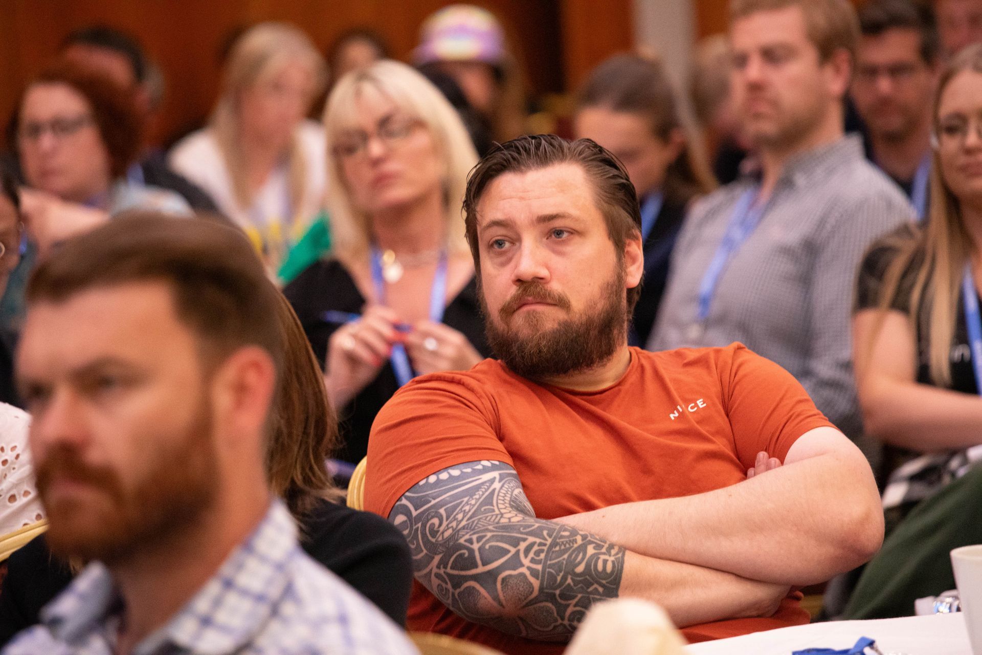 A man with a tattoo on his arm is sitting in a crowd of people.