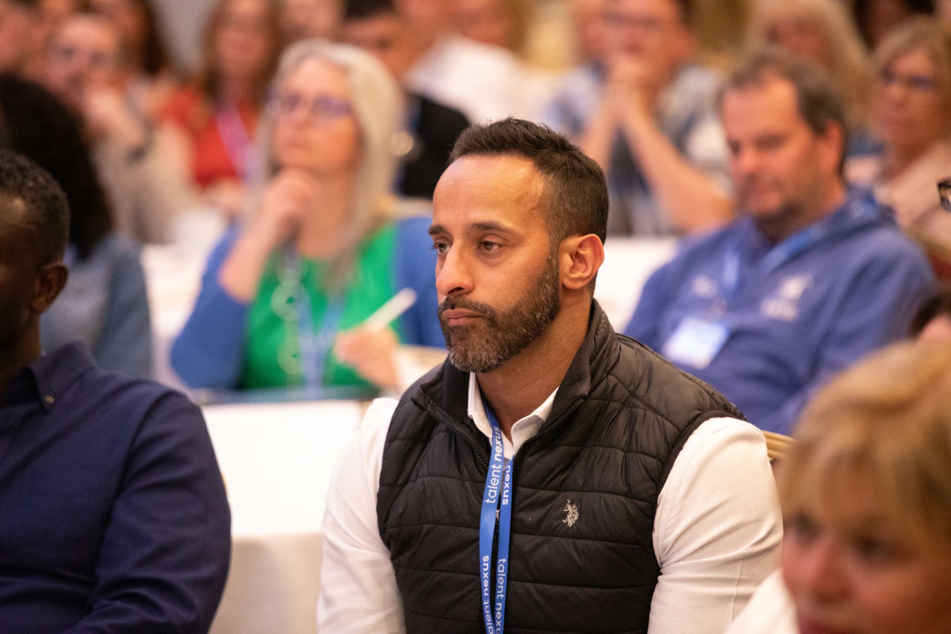 A man with a beard is sitting in a classroom with other people.