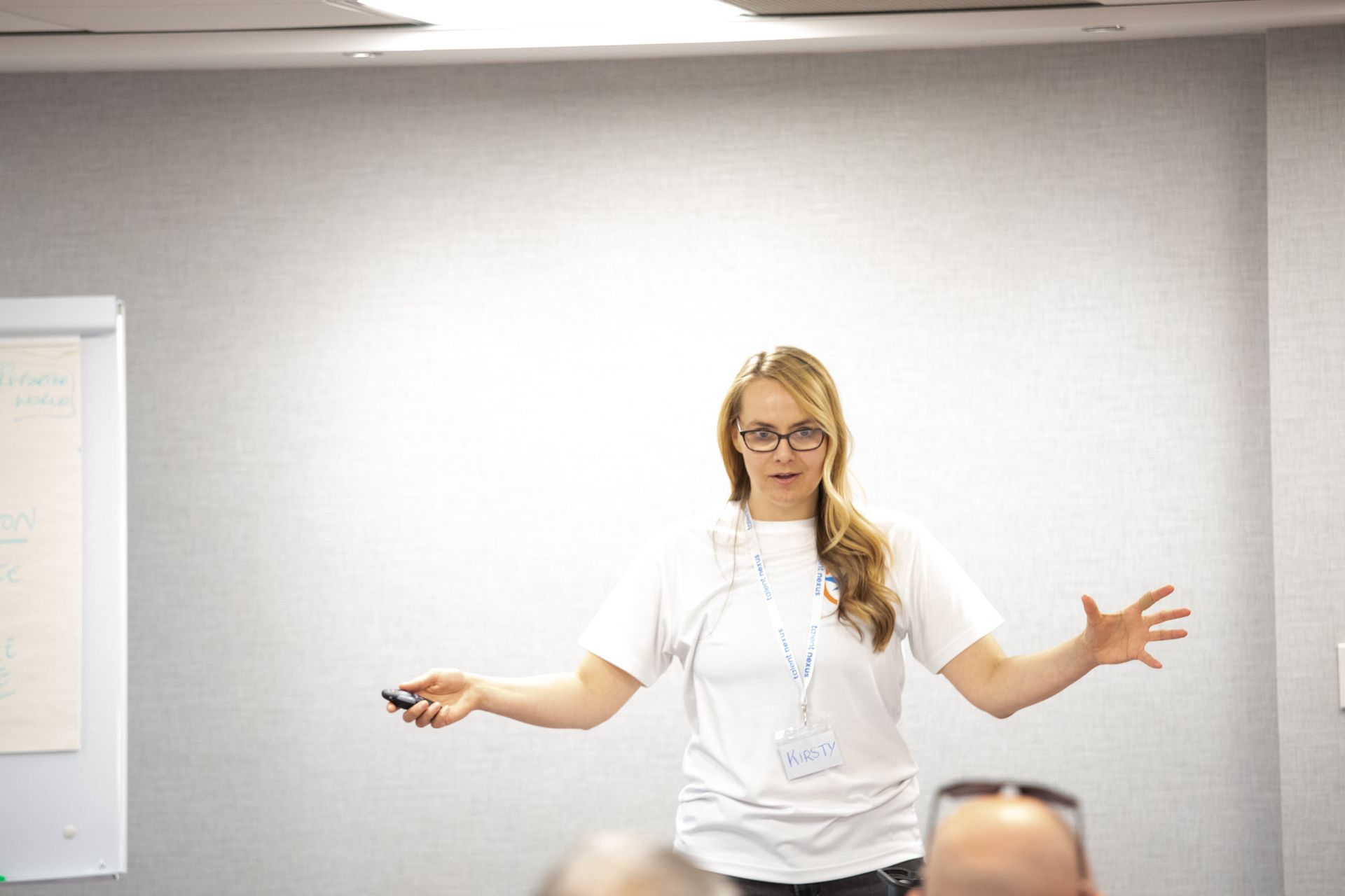 A woman wearing glasses is giving a presentation in front of a group of people.