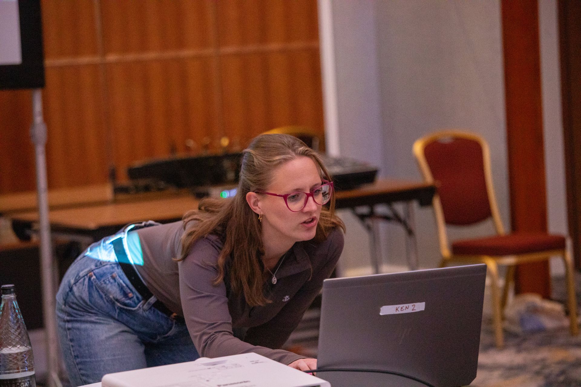 A woman wearing glasses is standing in front of a laptop computer.