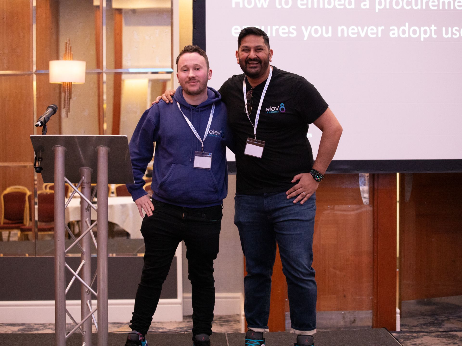 Two men are posing for a picture in front of a projector screen.