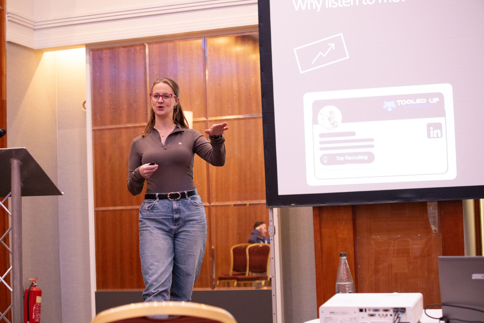 A woman is giving a presentation in front of a projector screen.