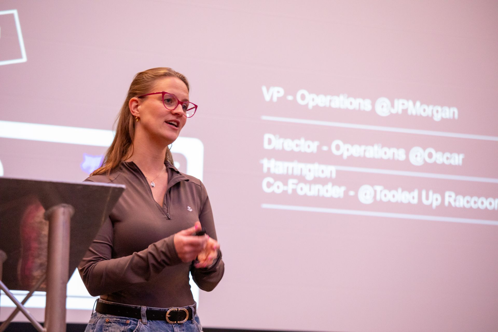 A woman wearing glasses is giving a presentation in front of a large screen.