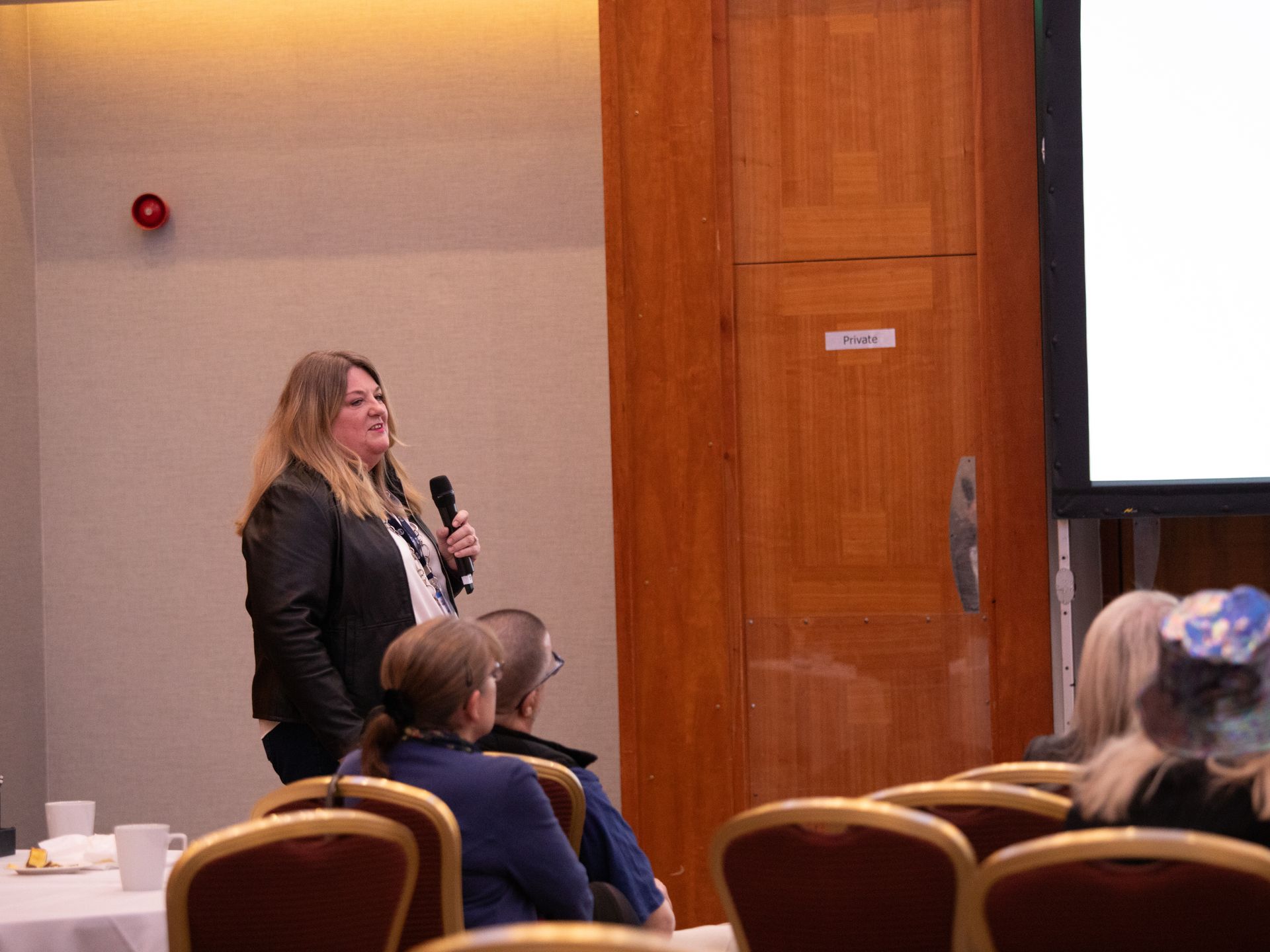 A woman is standing in front of a group of people holding a microphone.