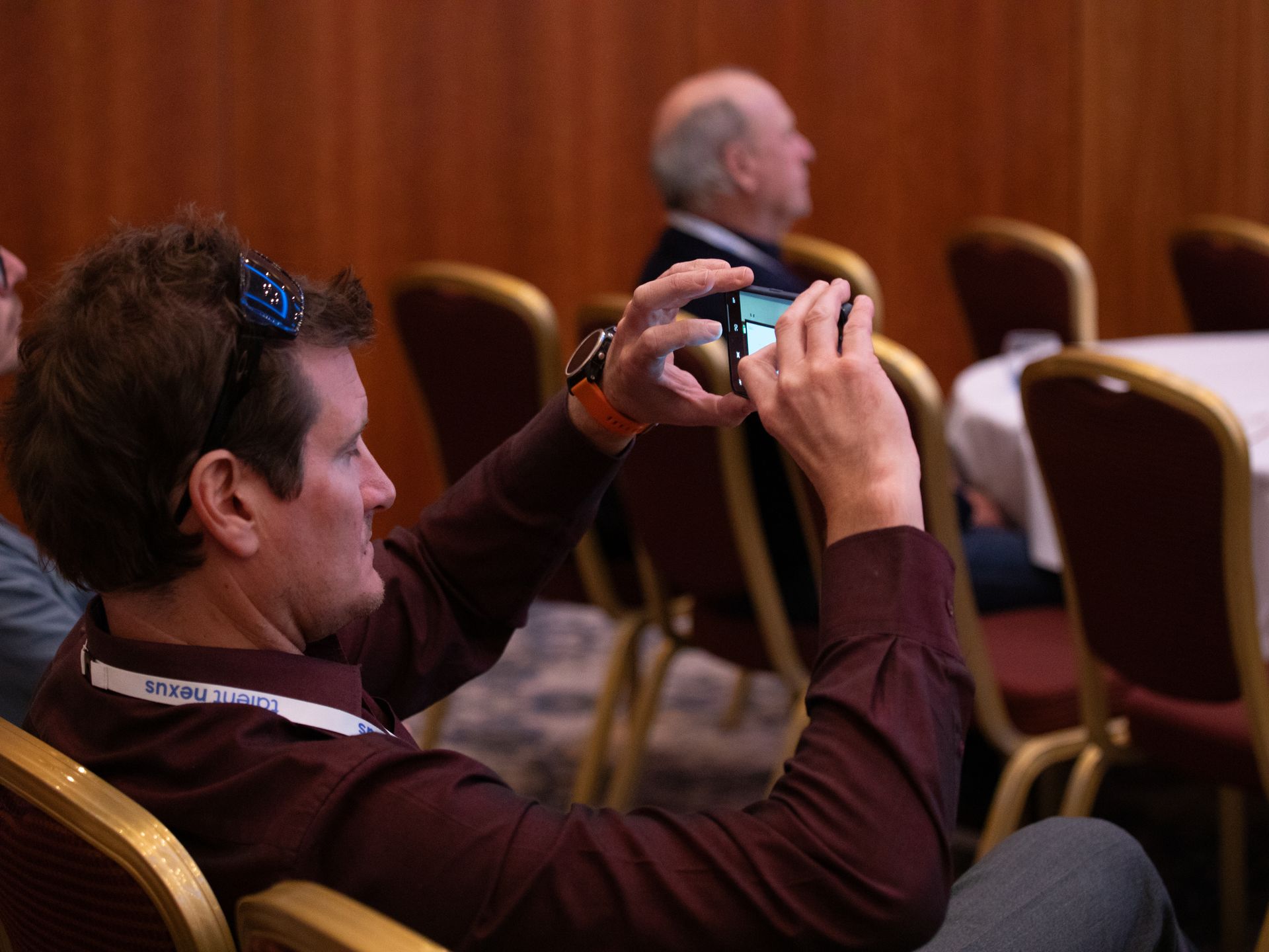A man is sitting in a chair taking a picture with his cell phone.