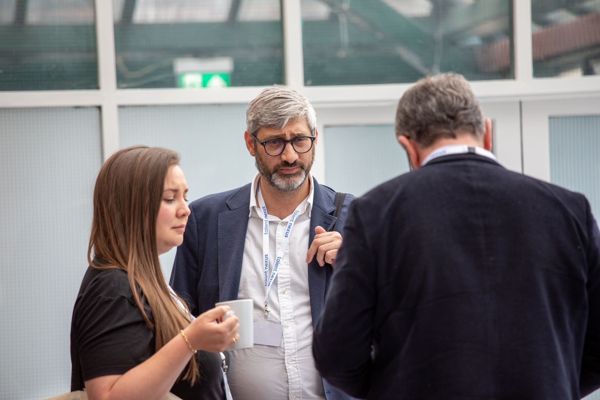 A man and a woman are talking to each other while a man holds a cup of coffee.