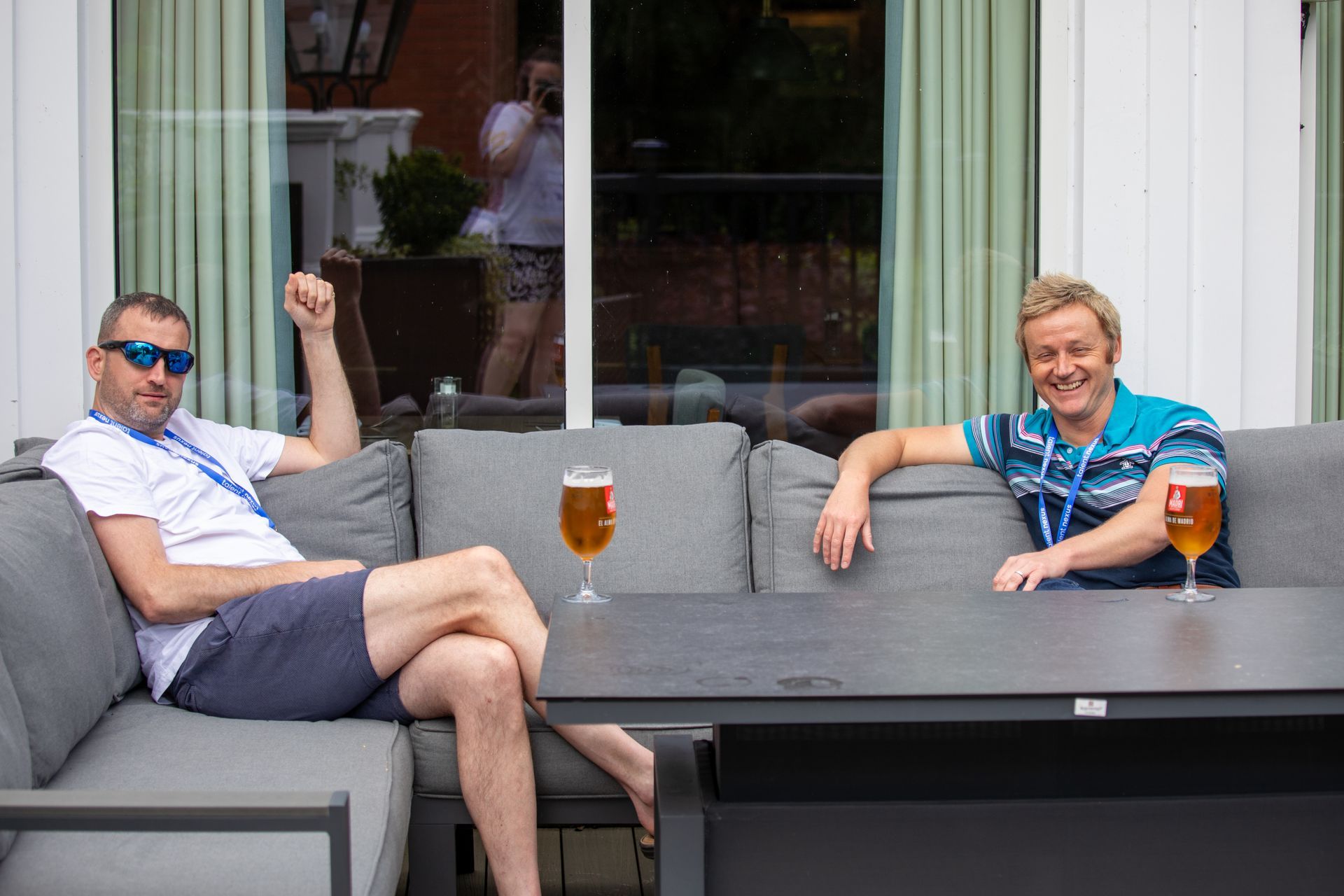 Two men are sitting on a couch and a table with glasses of beer.