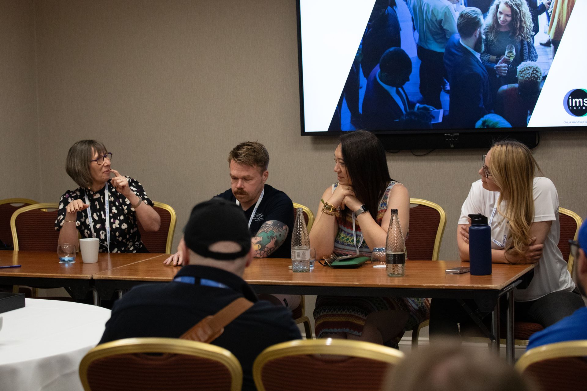 A group of people are sitting at a table in front of a large screen.