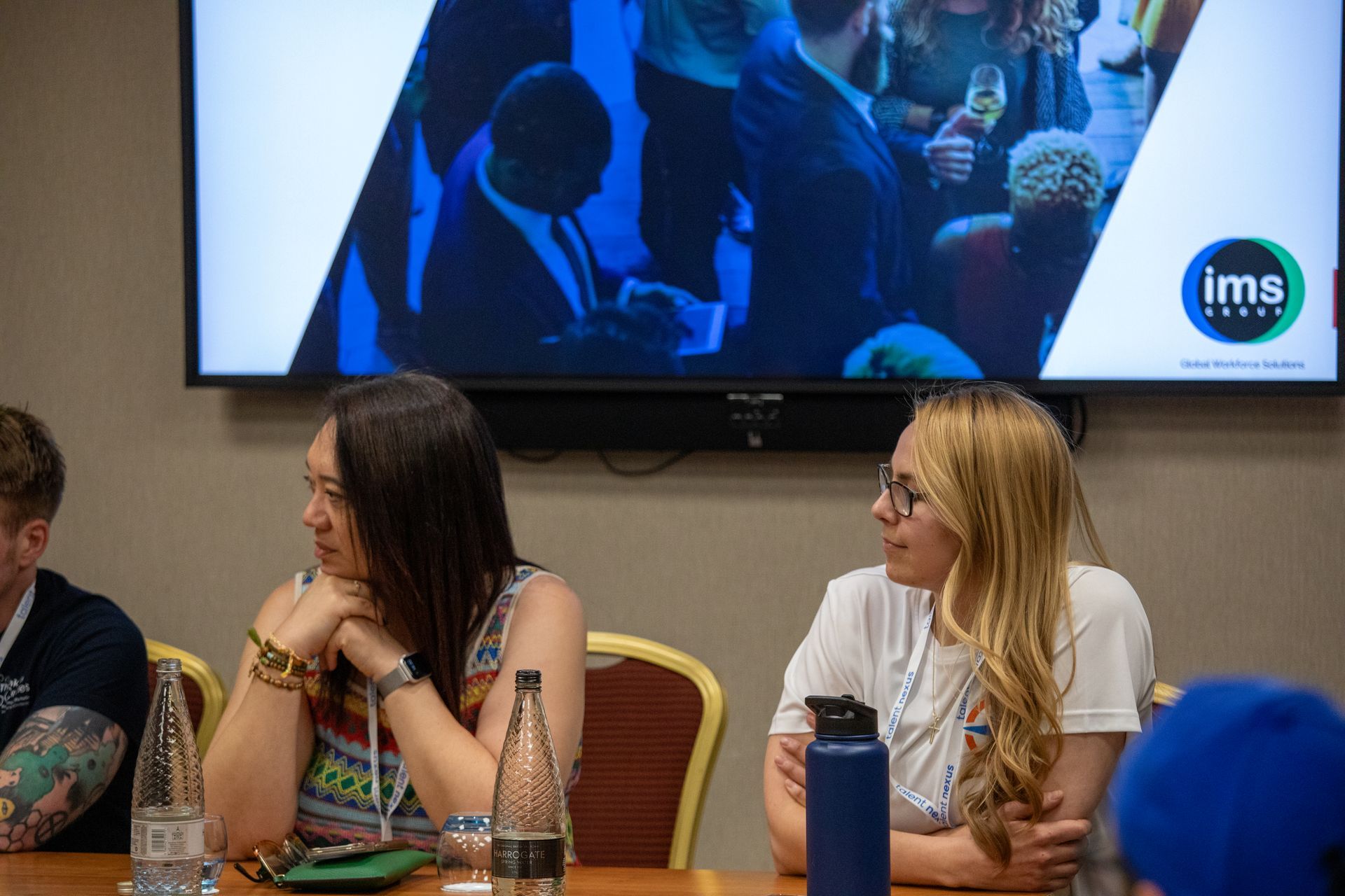 A group of people are sitting at a table in front of a large screen.