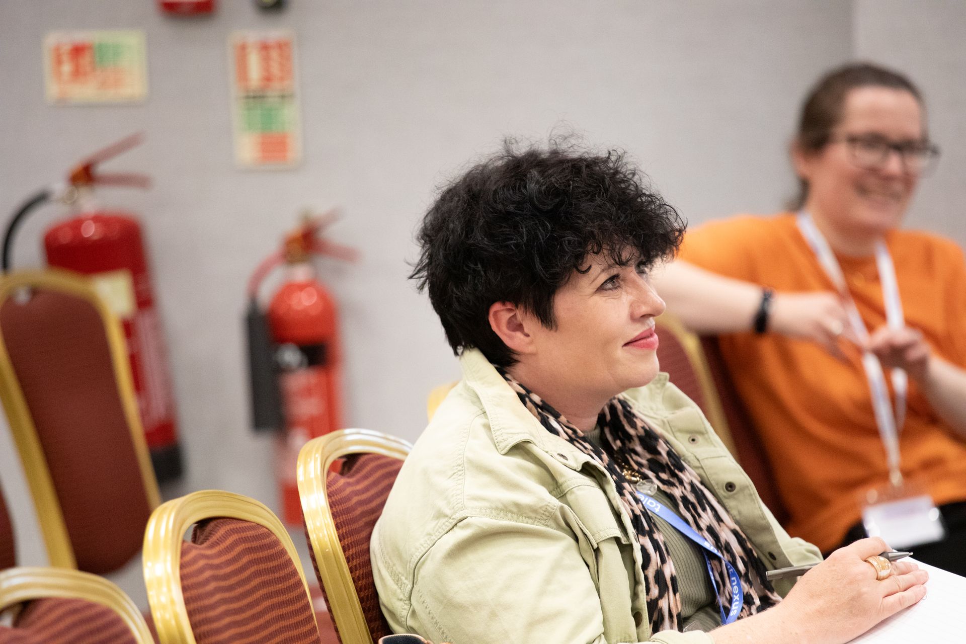 Two women are sitting in chairs in a room with fire extinguishers in the background.
