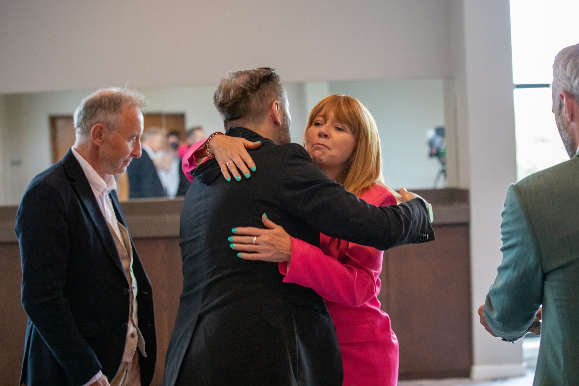 A woman in a pink dress is hugging a man in a black suit.