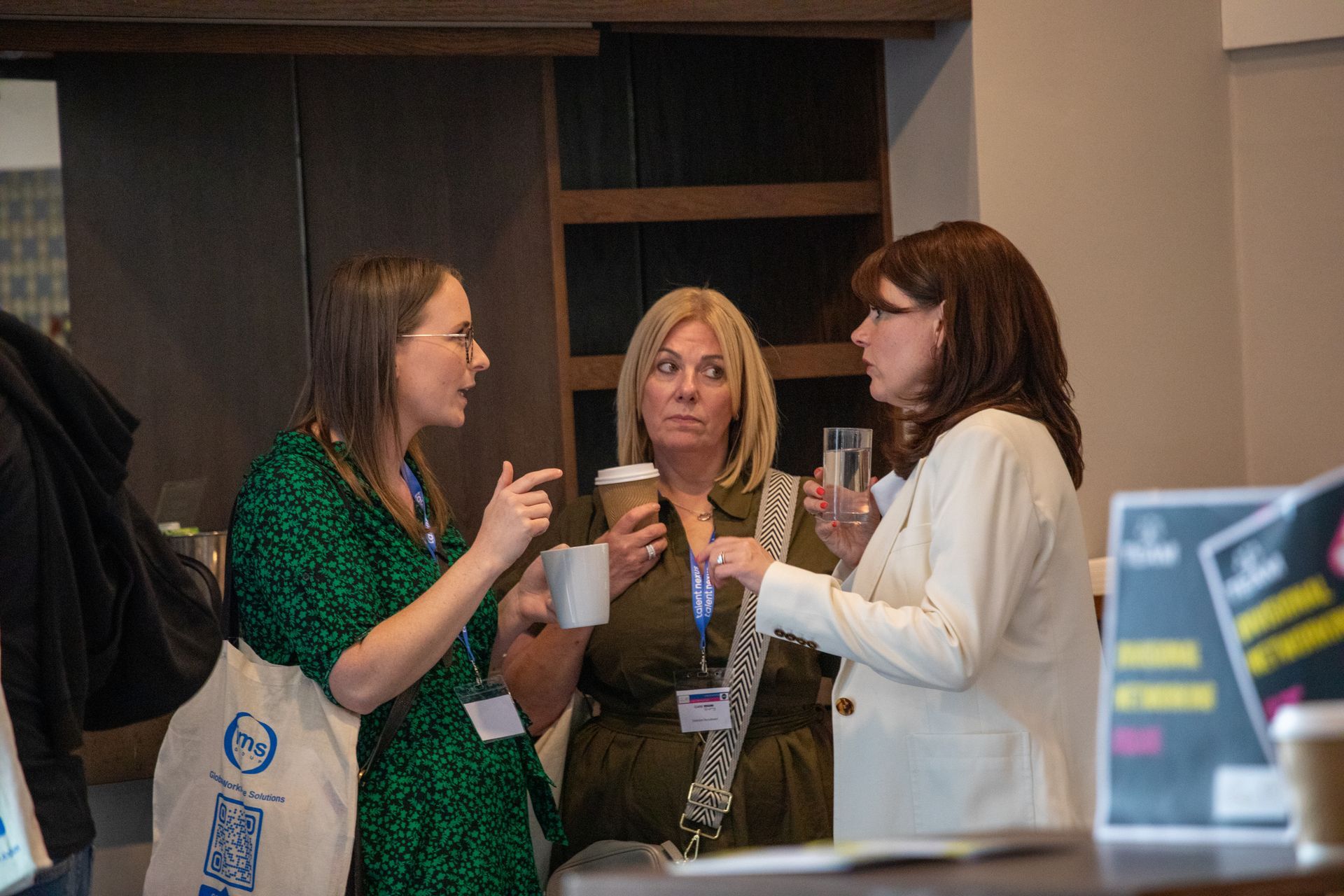 Three women are standing next to each other talking in a room.