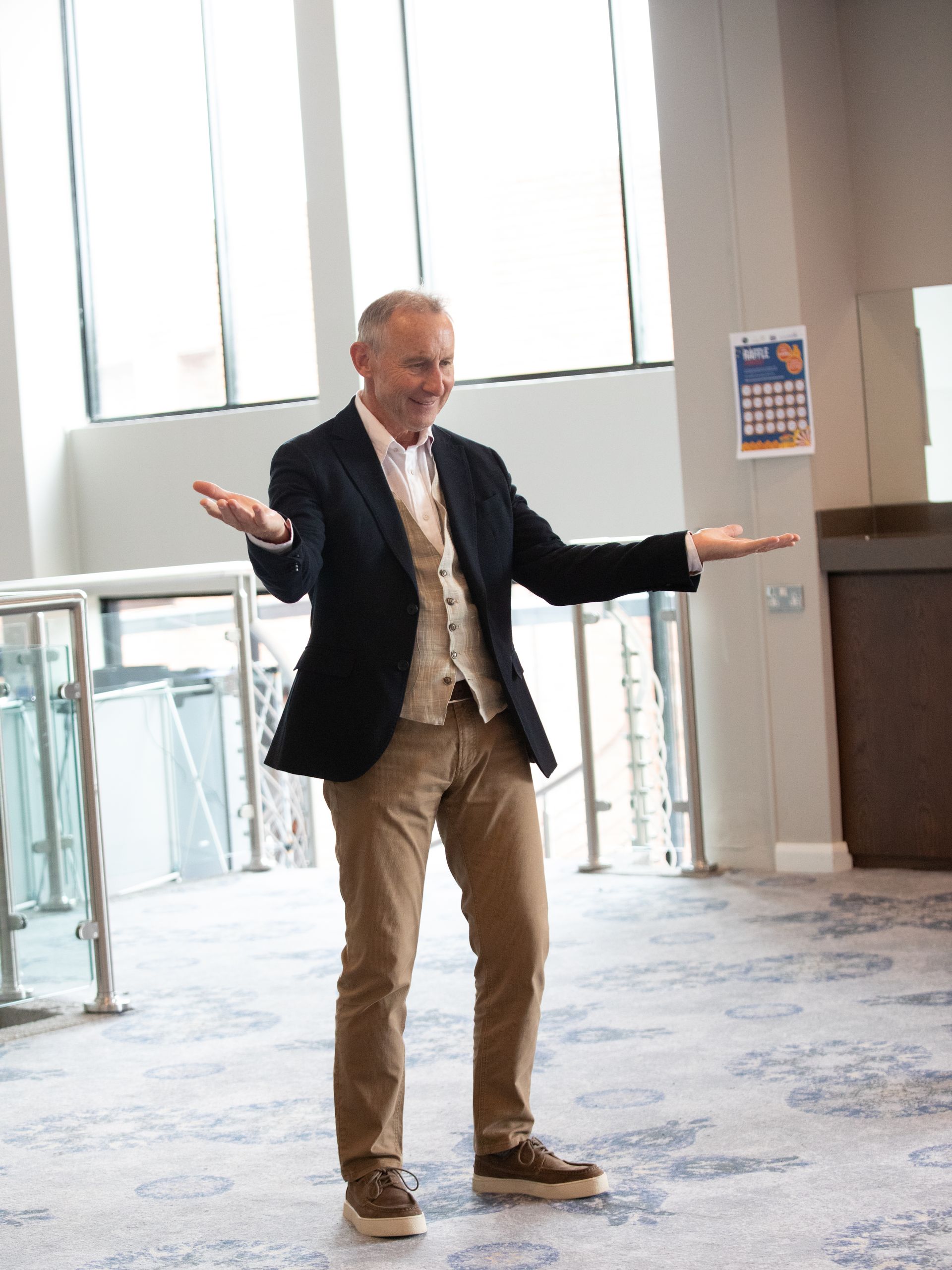 A man in a suit is standing in a room with his arms outstretched.