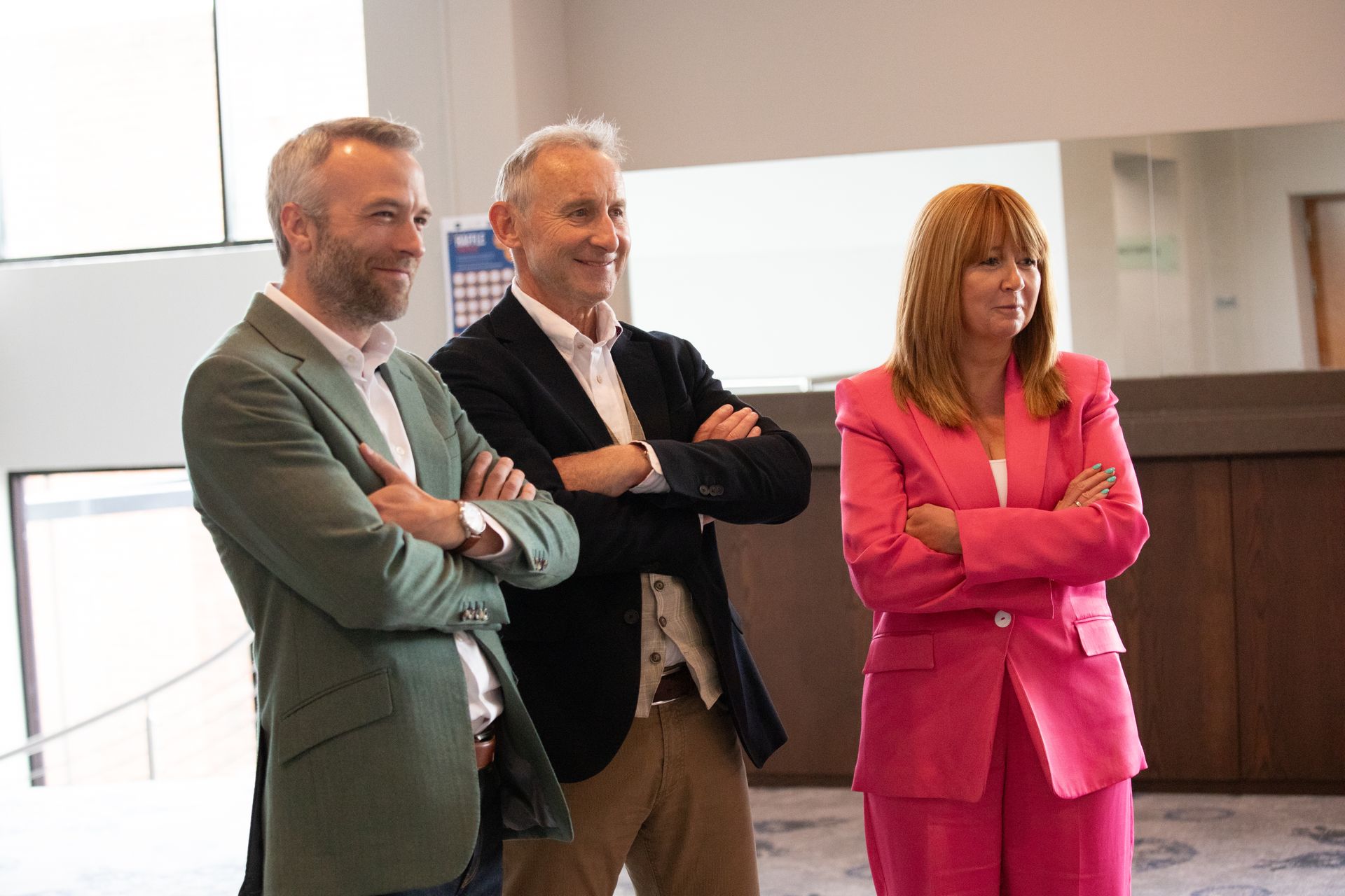 Three people are standing next to each other in a room with their arms crossed.