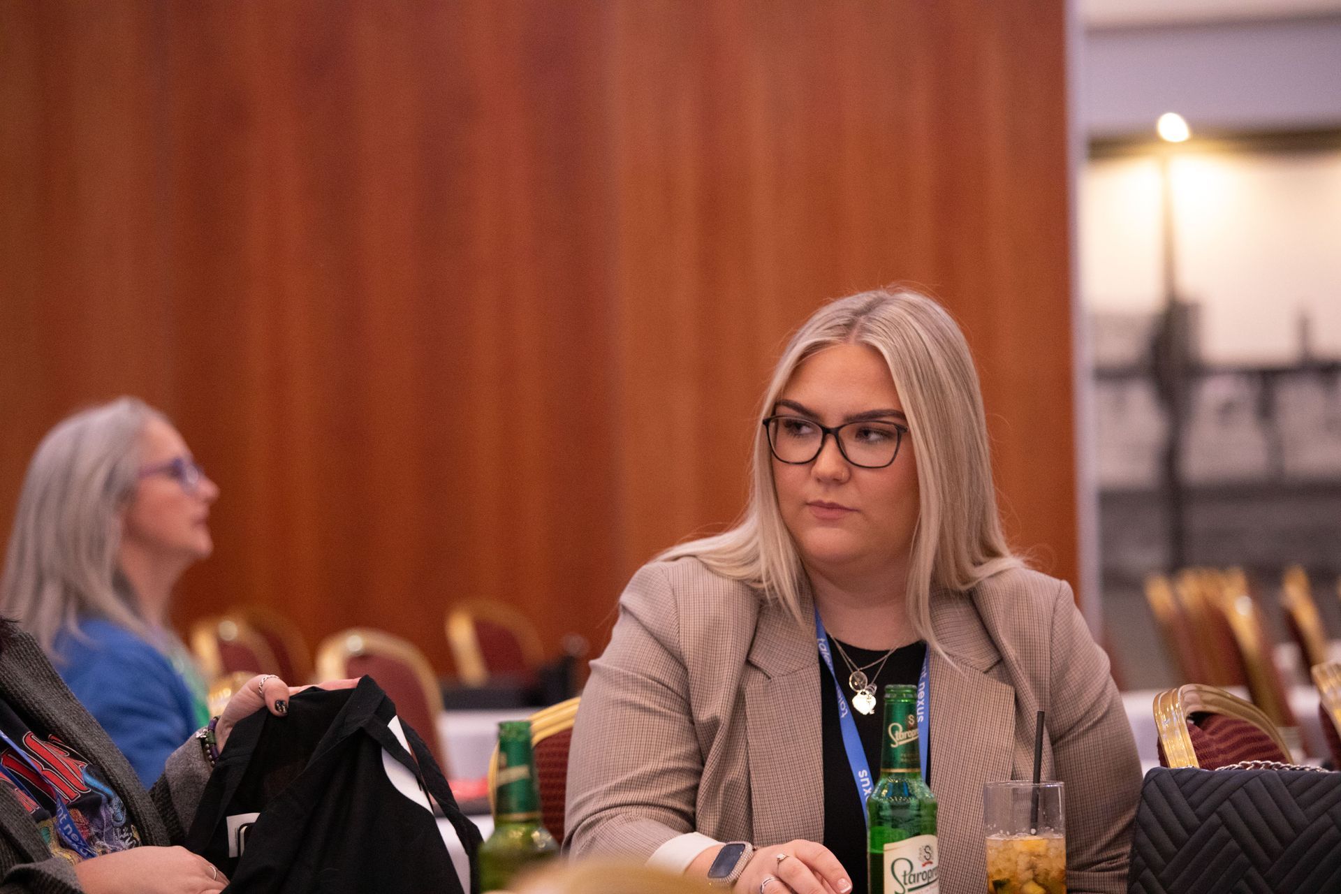 A woman is sitting at a table with a bottle of beer.