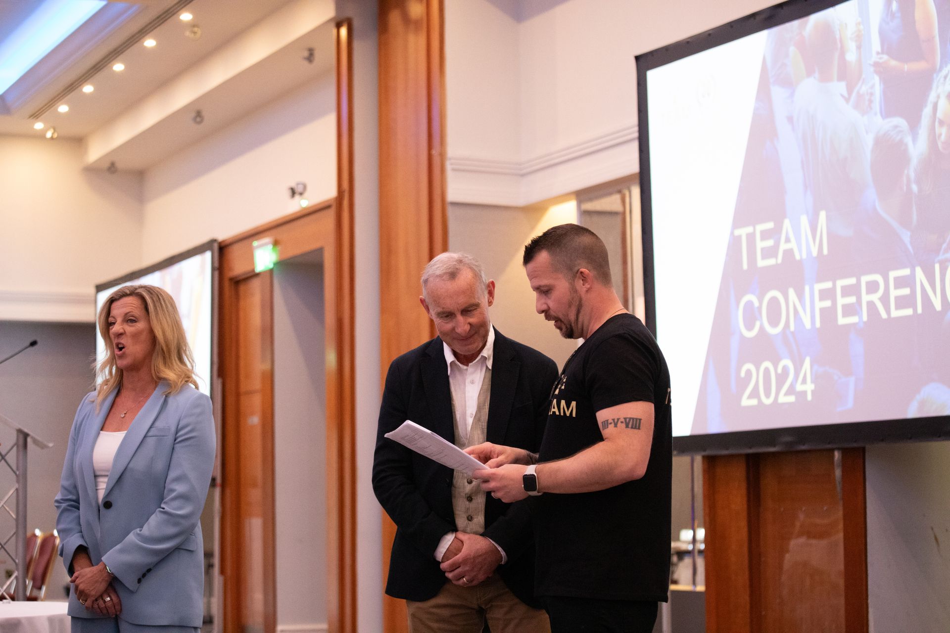 A group of people are standing in front of a large screen.