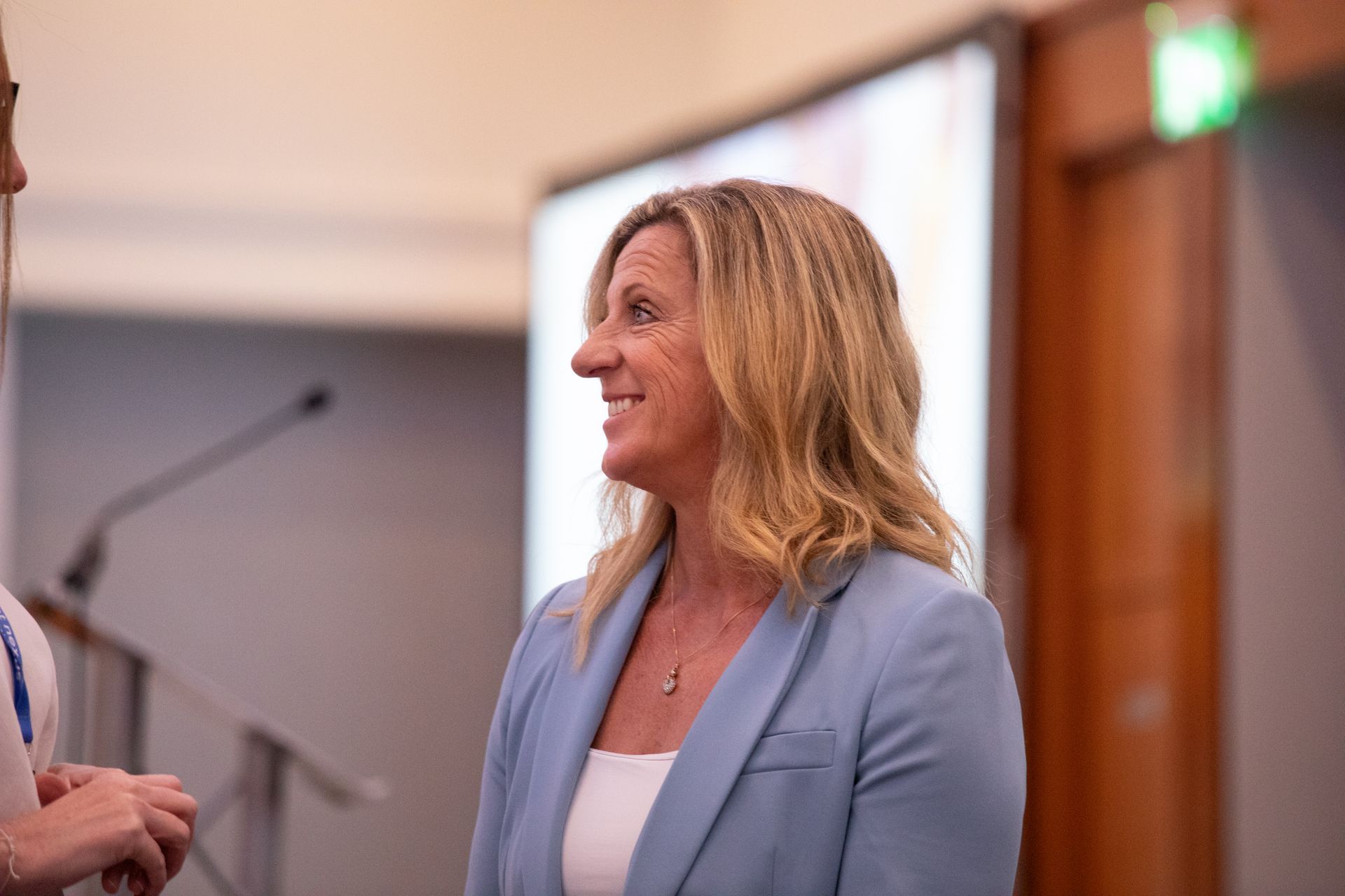 A woman in a blue jacket is talking to another woman in a room.
