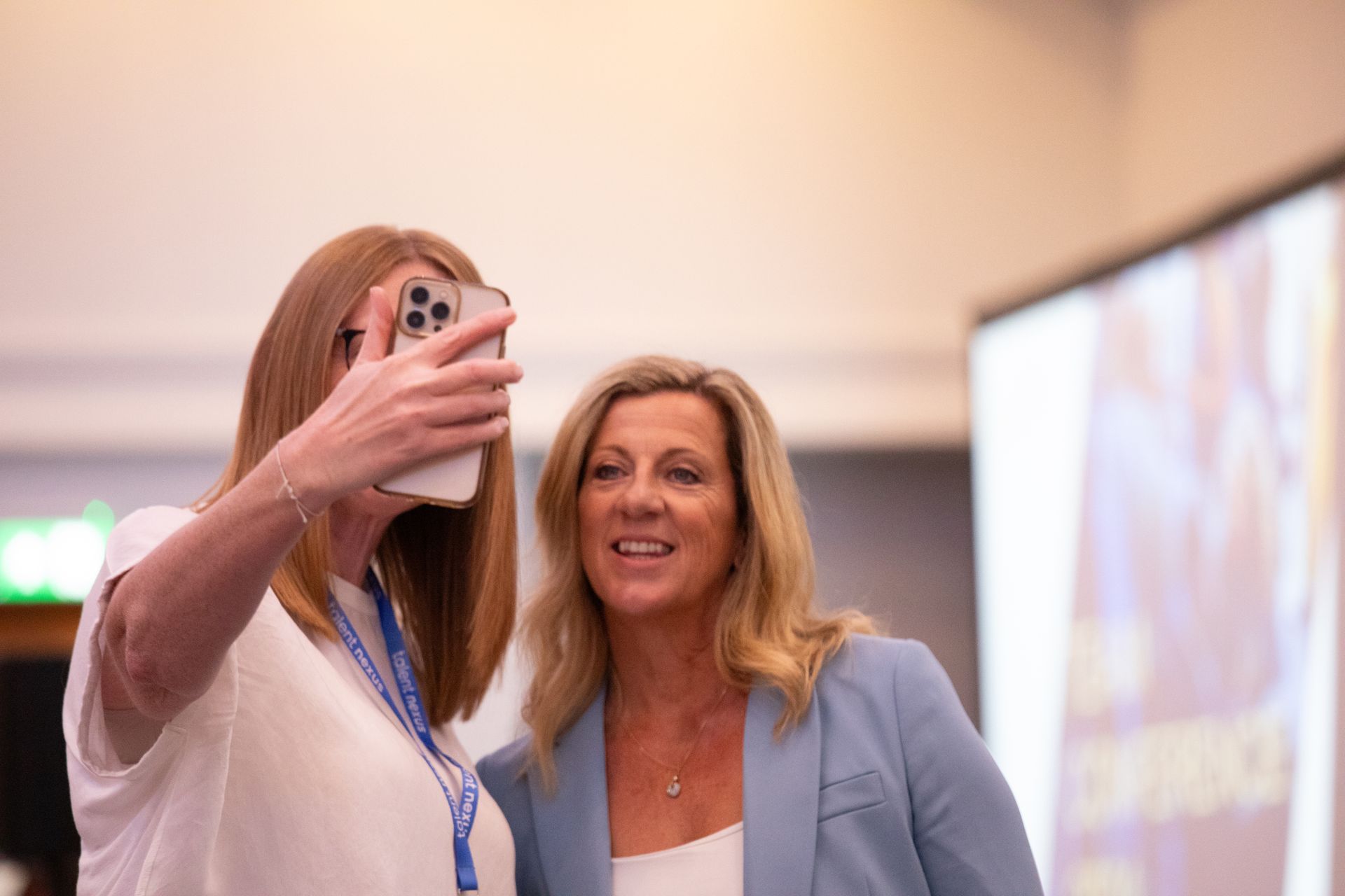 Two women are taking a selfie with their cell phones.