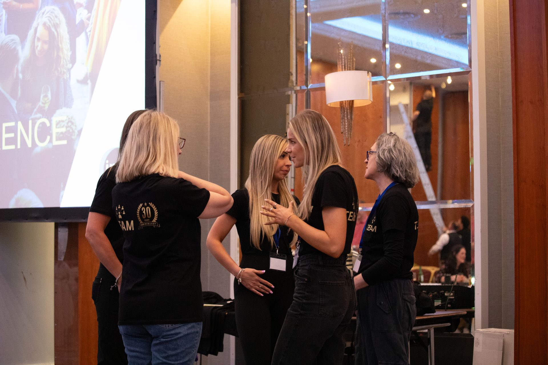 A group of women are standing in a room talking to each other.