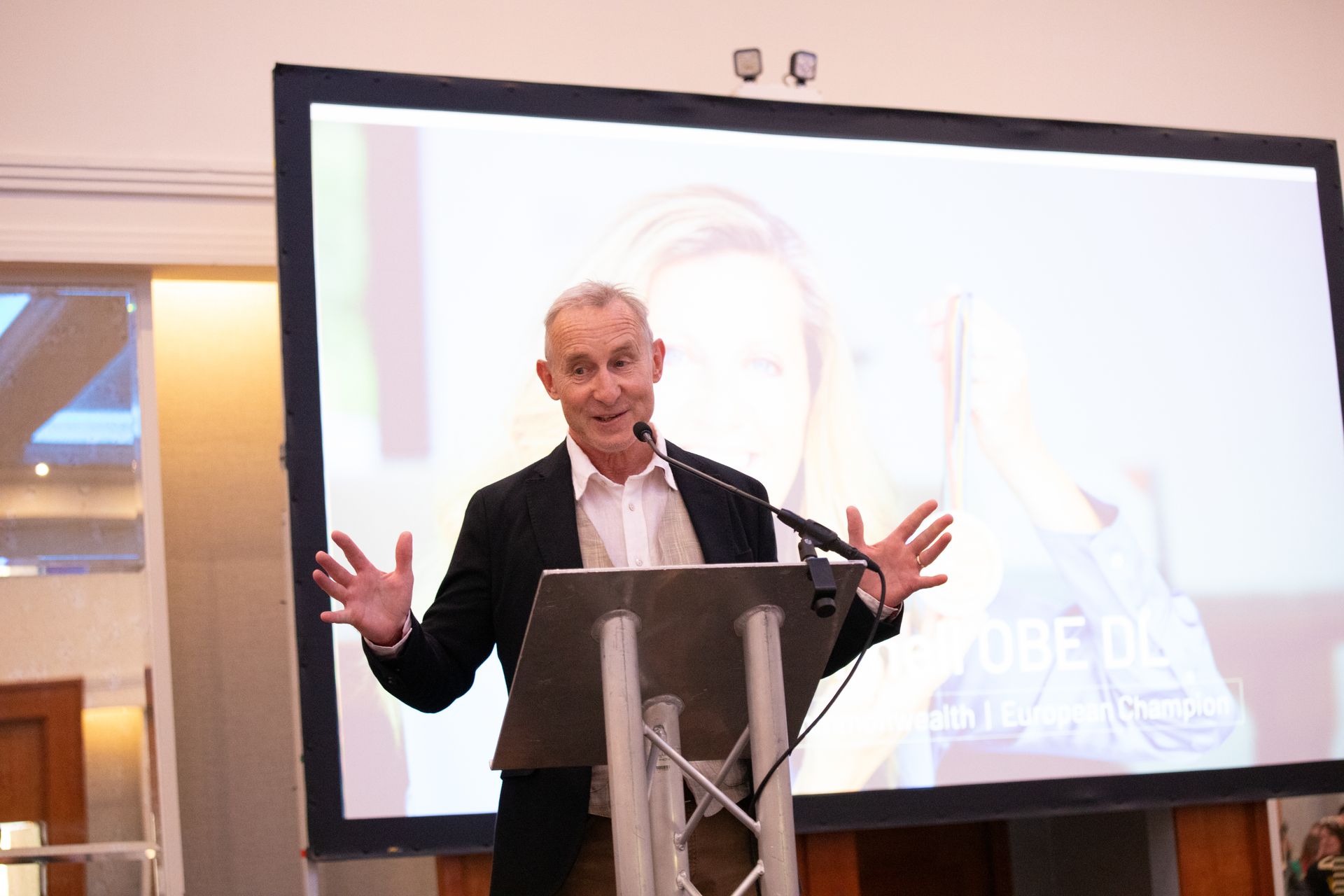 A man is giving a speech at a podium in front of a large screen.