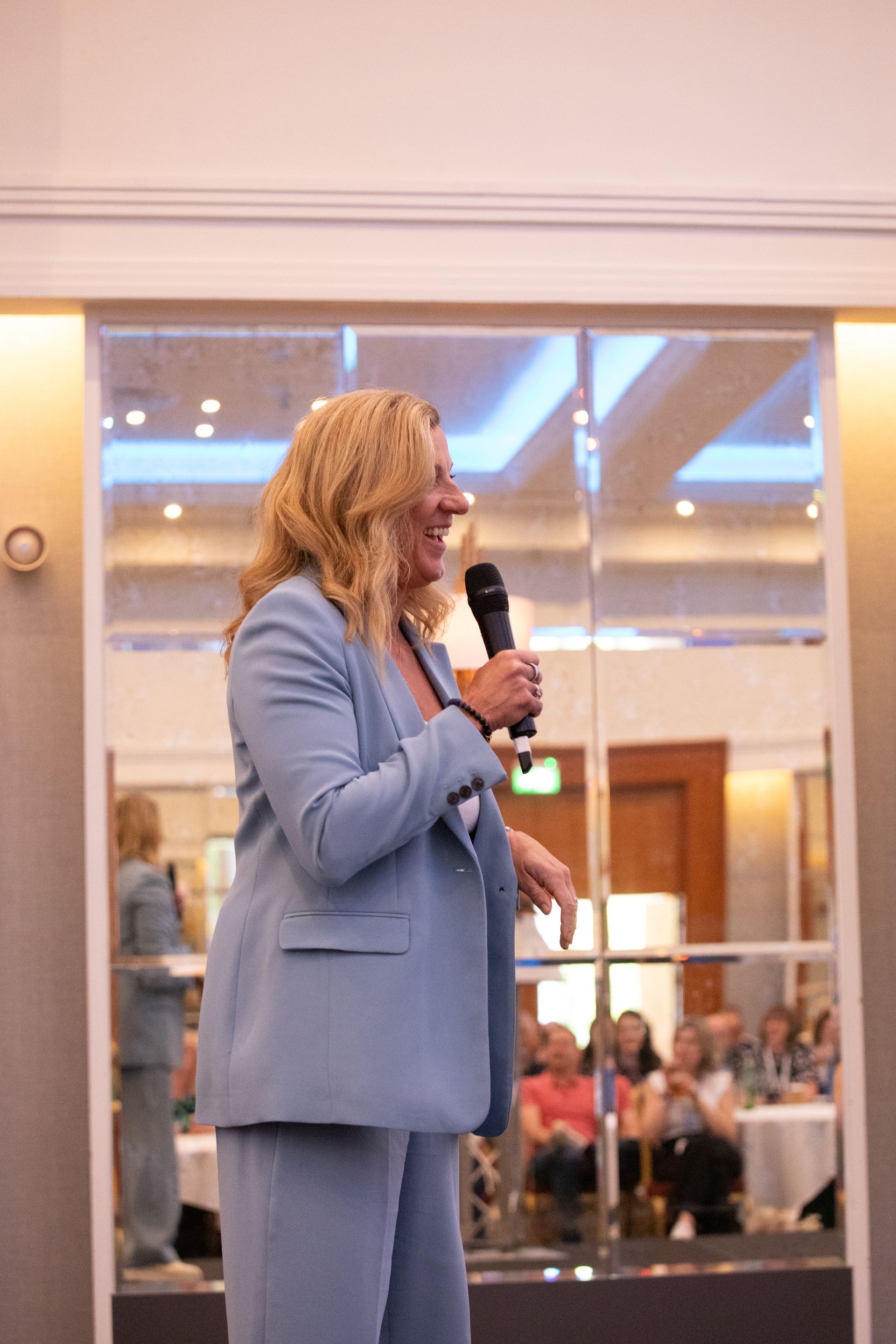 A woman in a blue suit is holding a microphone in a room.