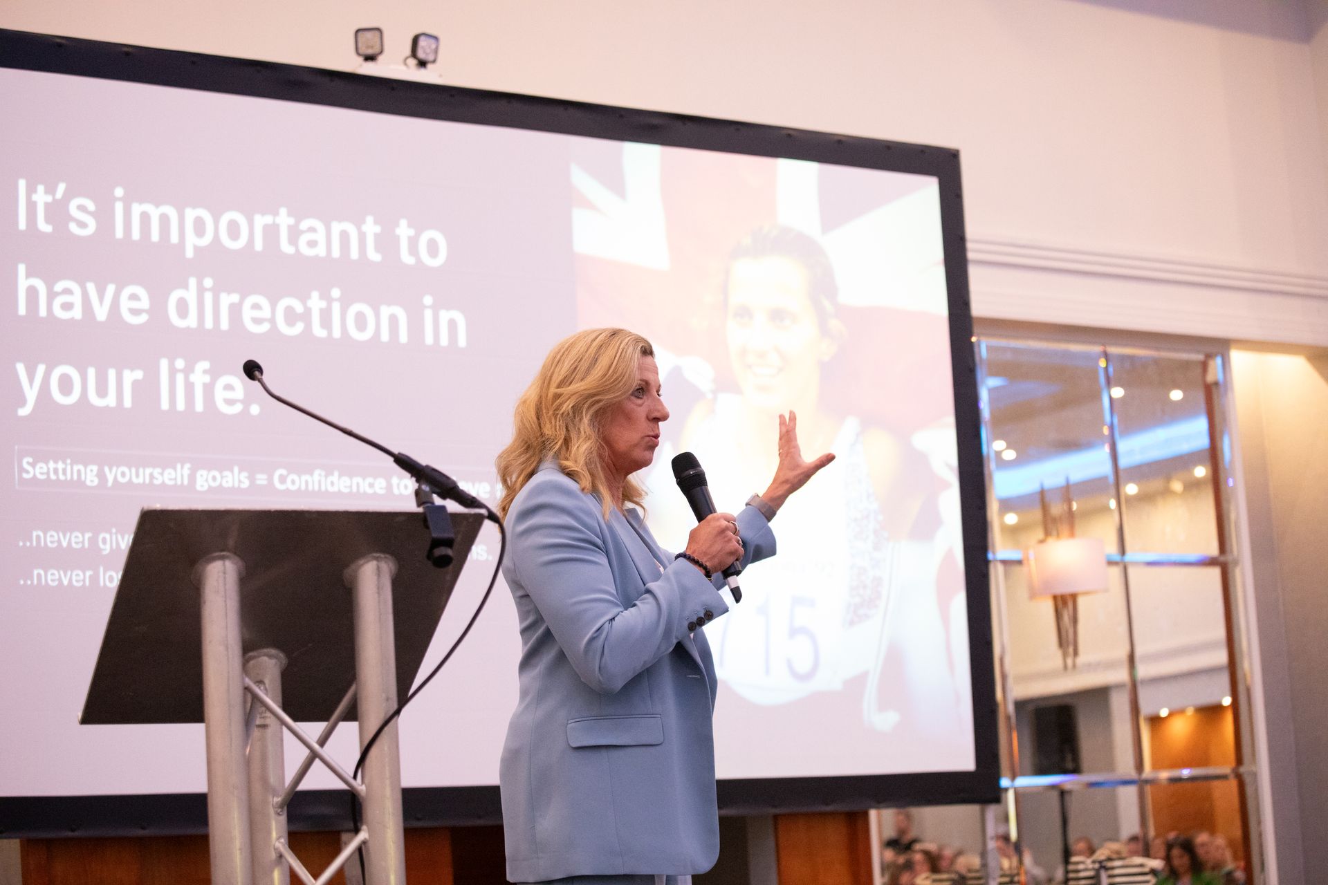 A woman is giving a speech in front of a screen that says `` it 's important to have direction in your life ''.
