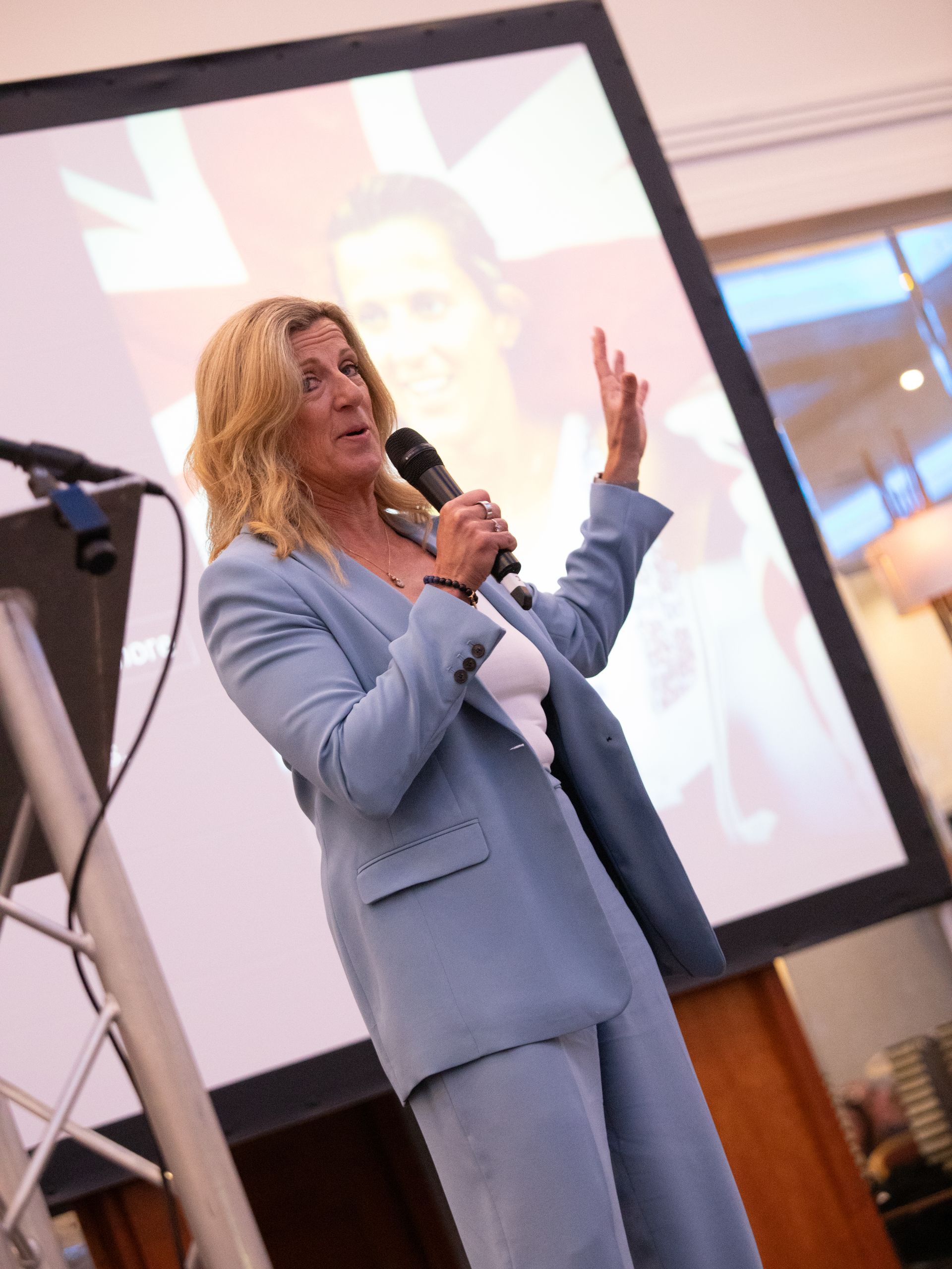 A woman in a blue suit is speaking into a microphone