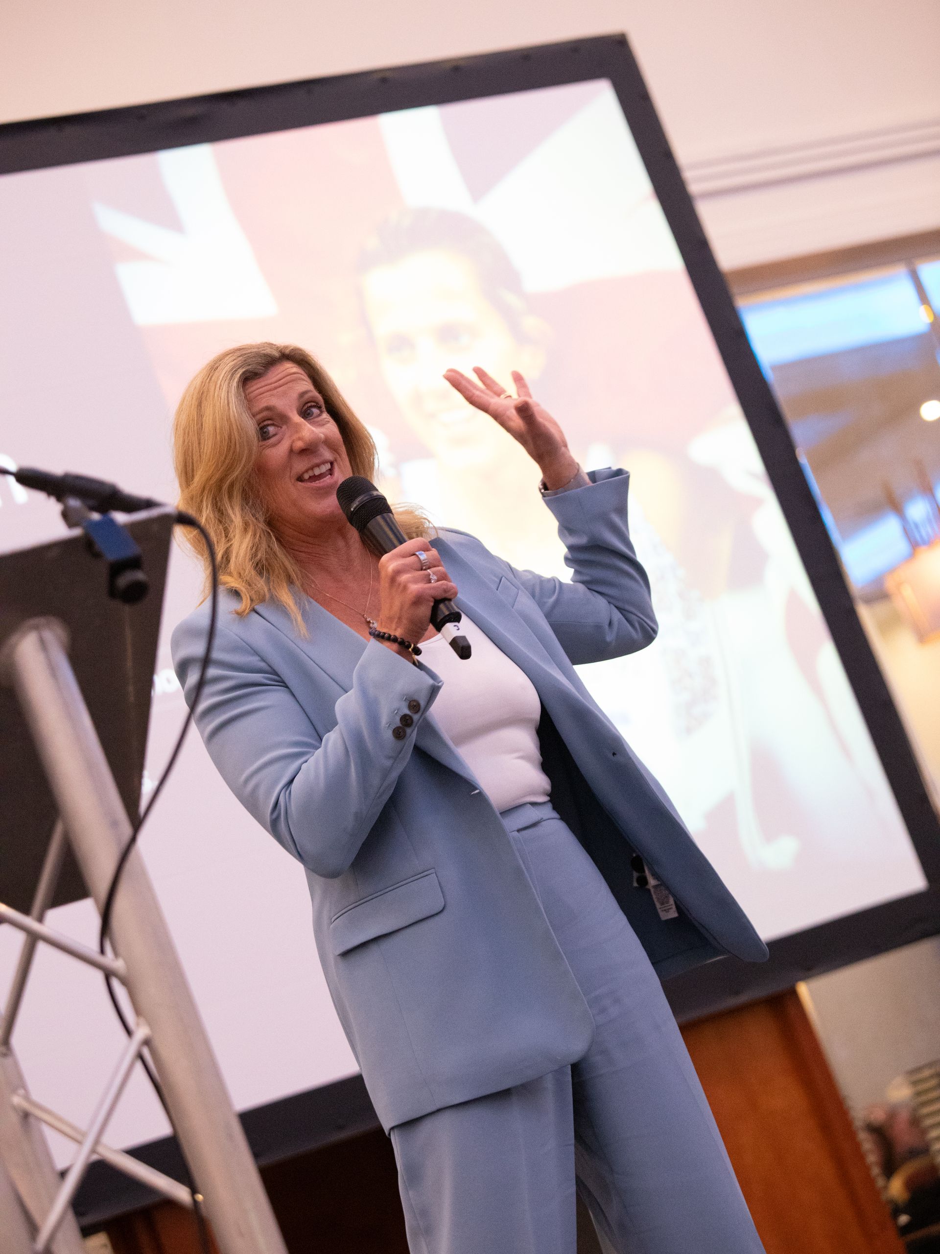 A woman in a blue suit is speaking into a microphone.