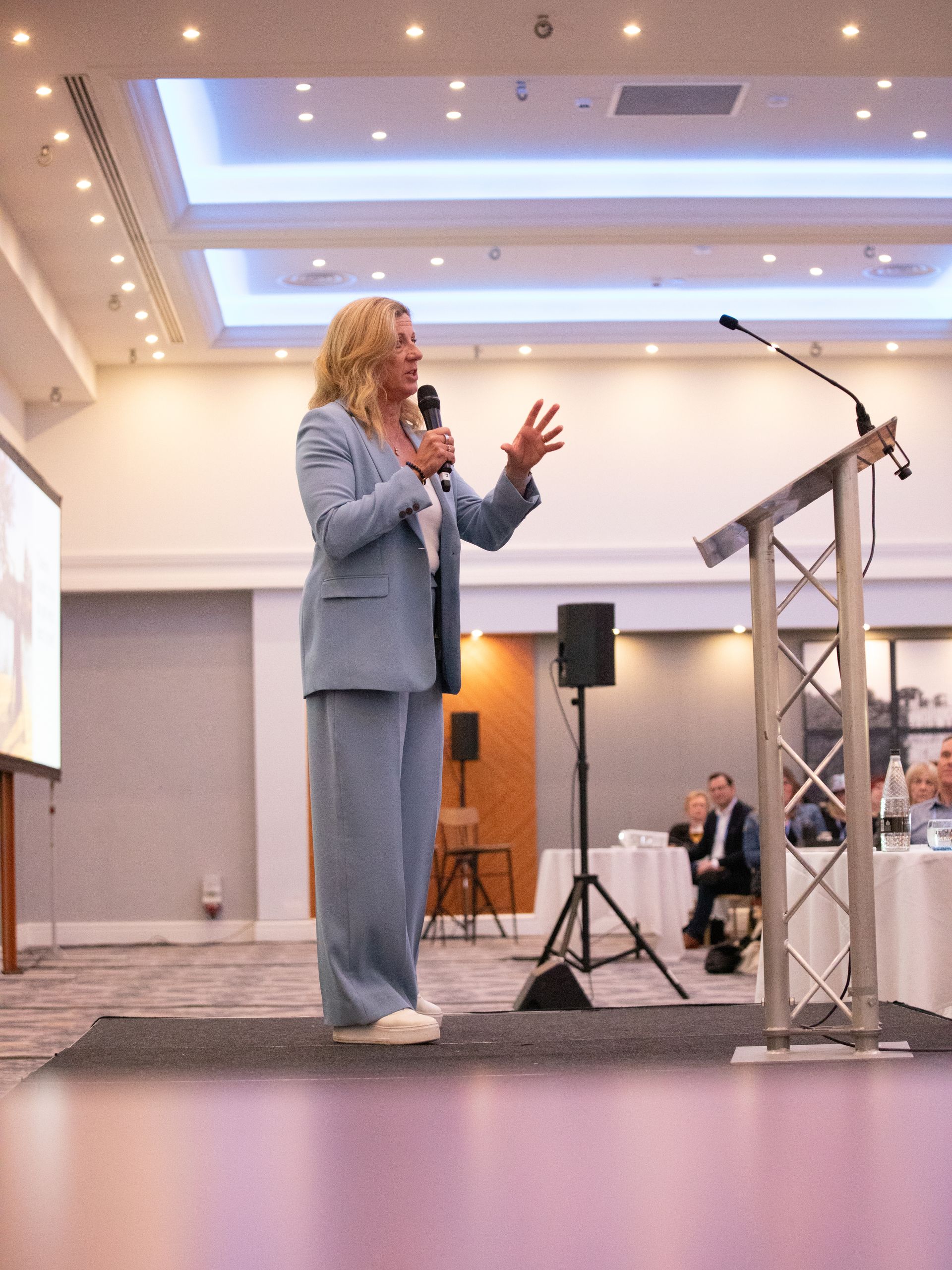 A woman in a blue suit is standing at a podium giving a speech.