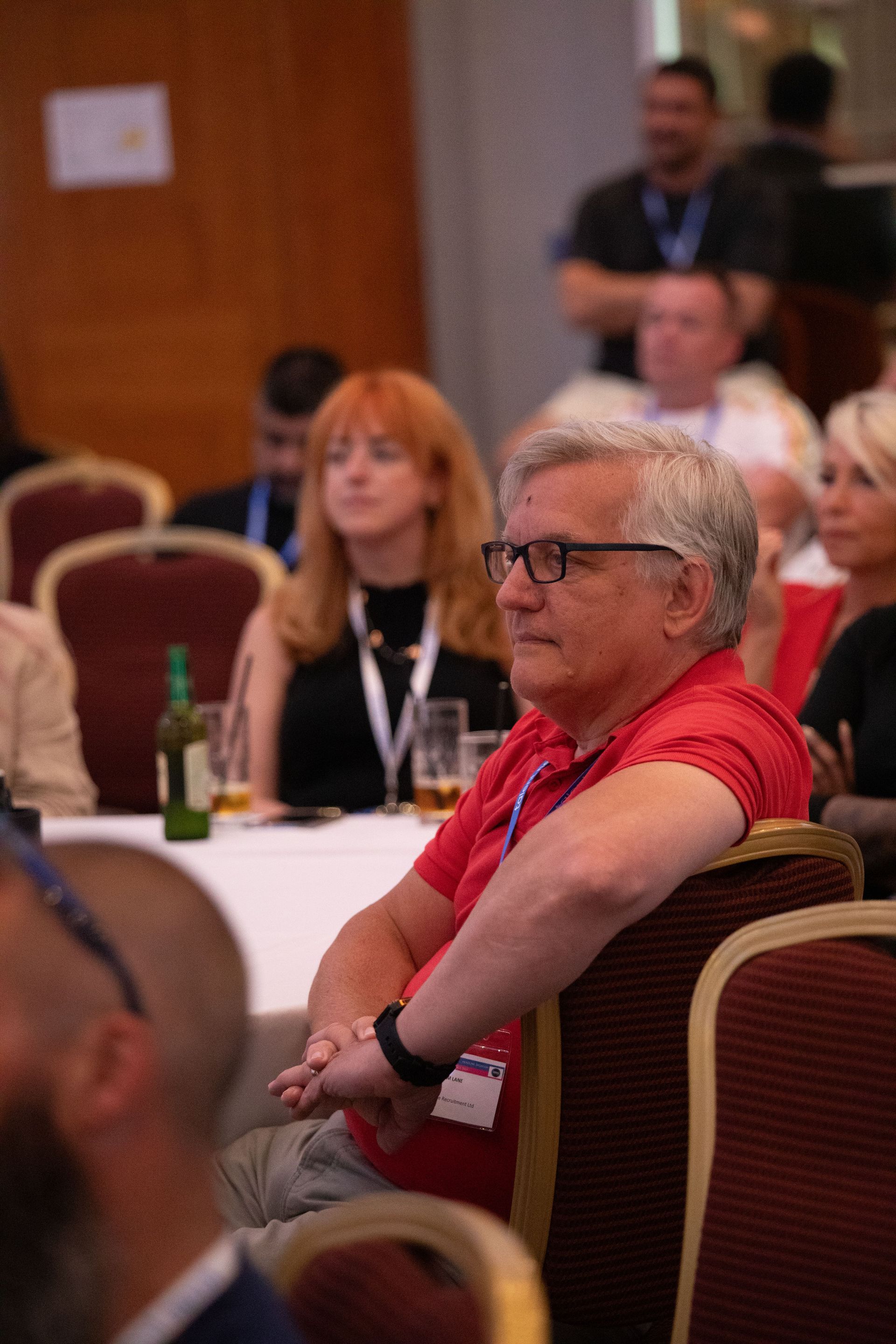 A man in a red shirt is sitting in a chair at a conference.