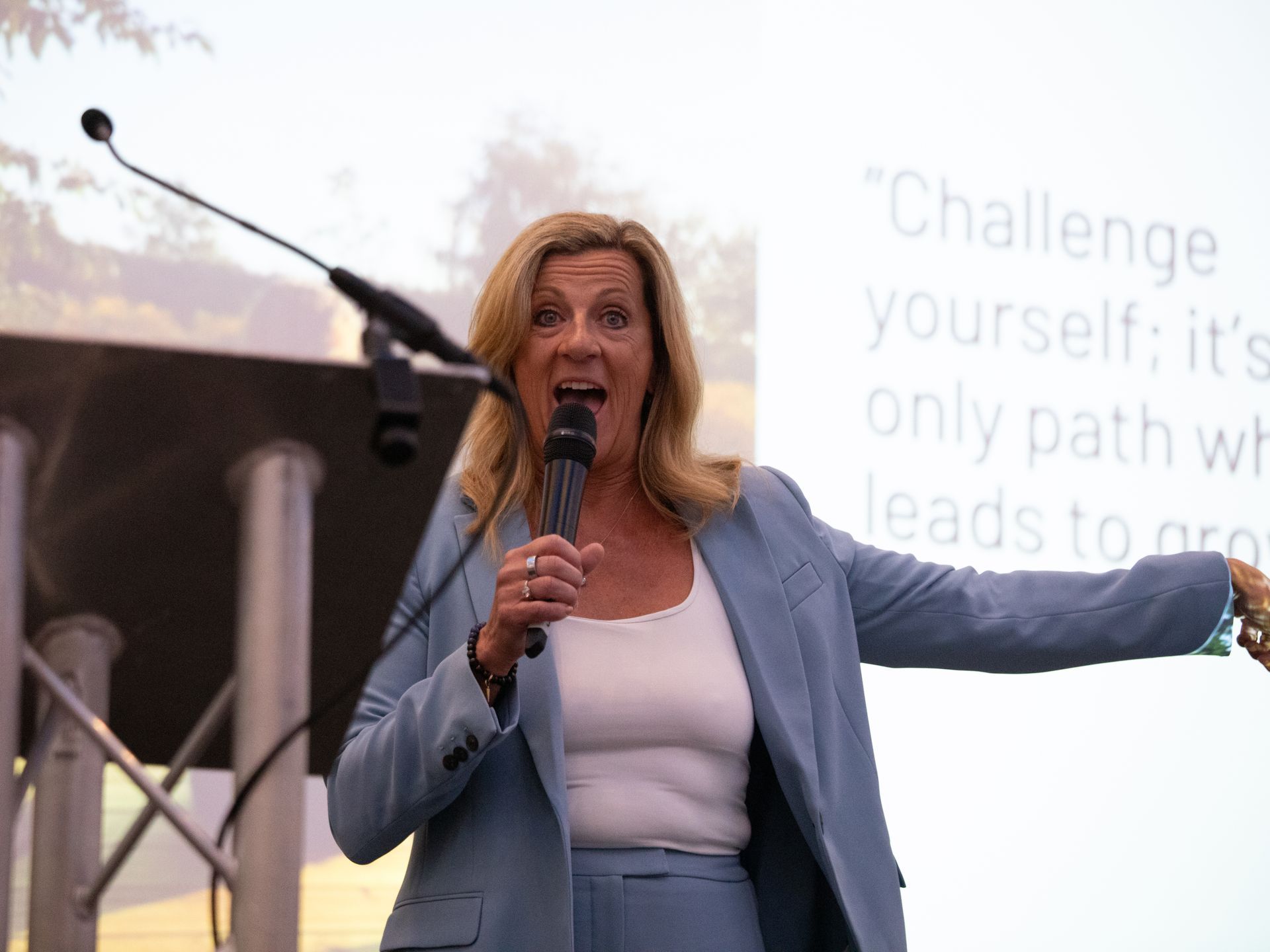 A woman in a blue suit is speaking into a microphone