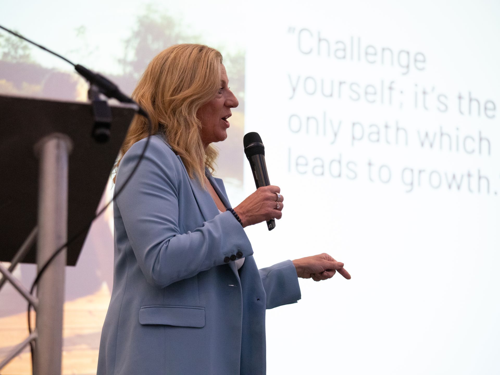 A woman in a blue jacket is speaking into a microphone