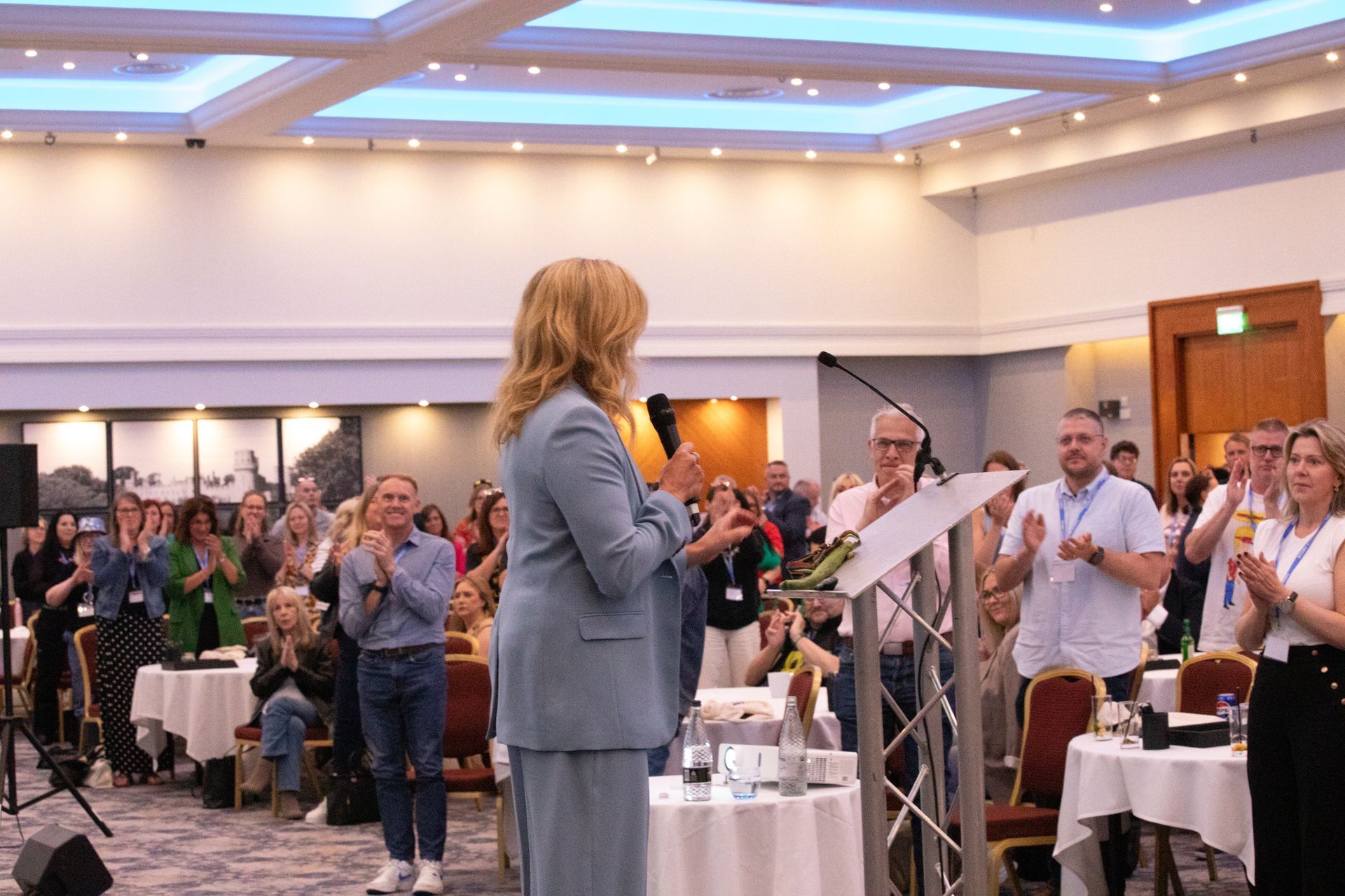 A woman is giving a speech at a podium in front of a crowd of people.