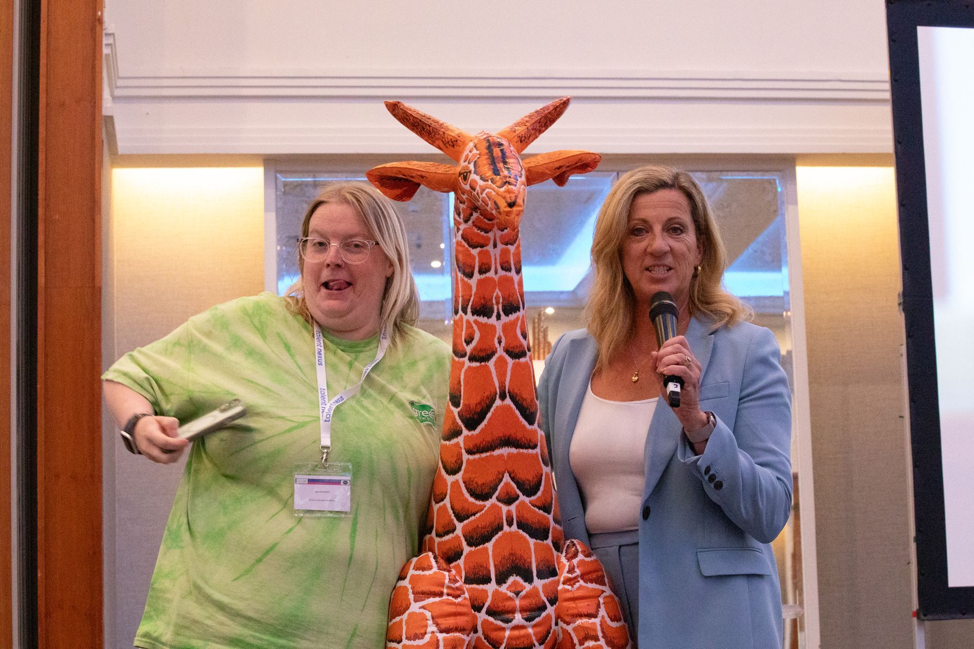 Two women are standing next to a stuffed giraffe.