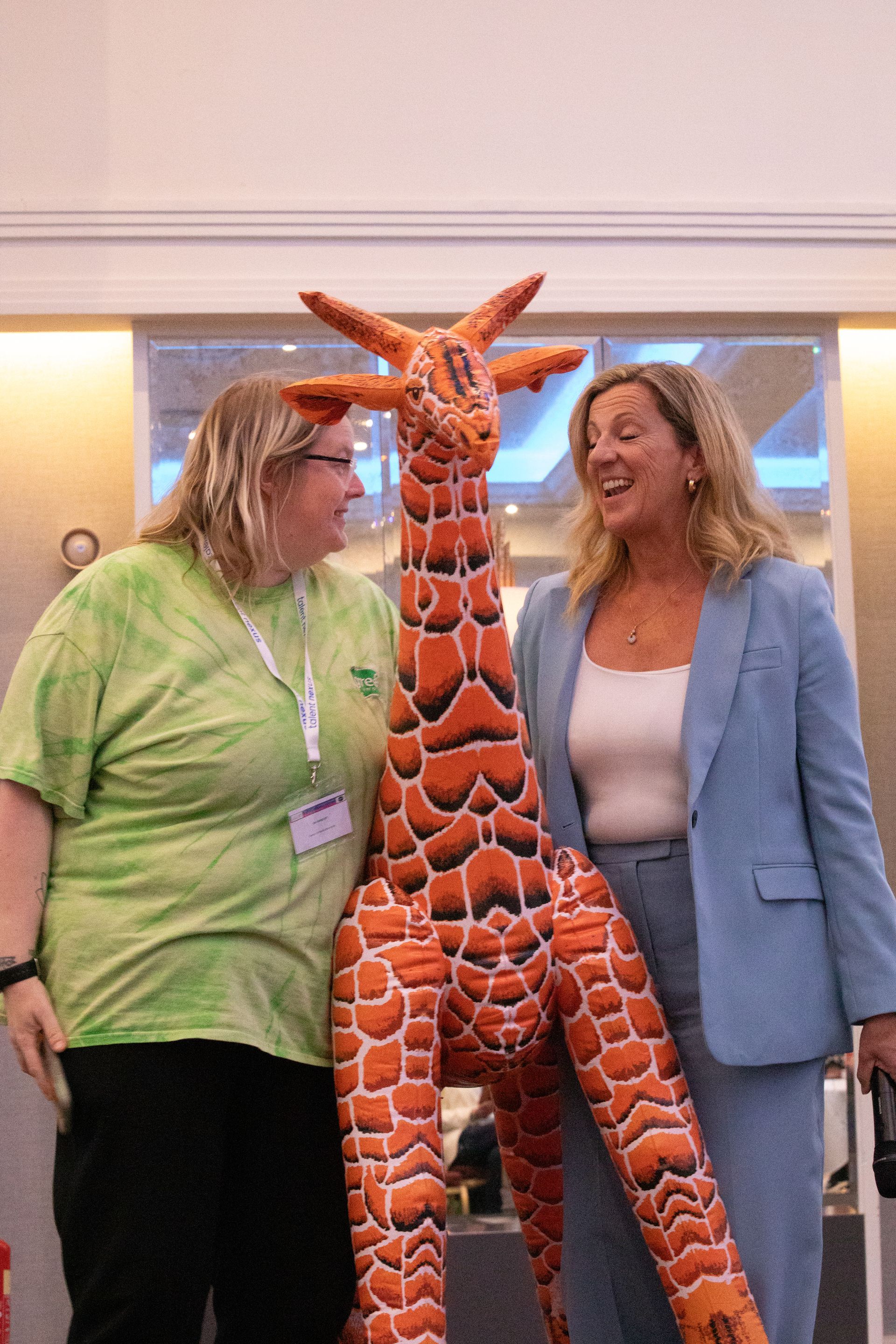 Two women are standing next to a stuffed giraffe.