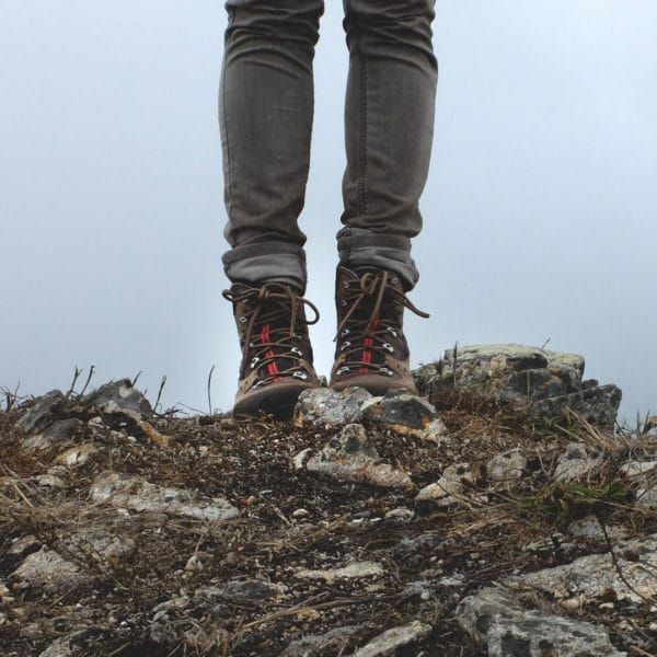 A person wearing hiking boots is standing on a rocky hillside