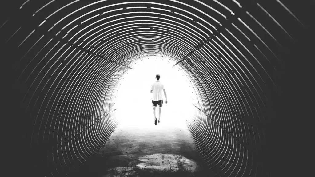 A man is walking through a tunnel with a light at the end.