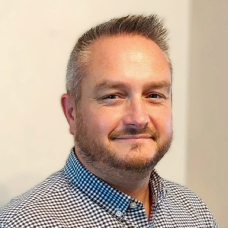 A man in a grey shirt is smiling for the camera