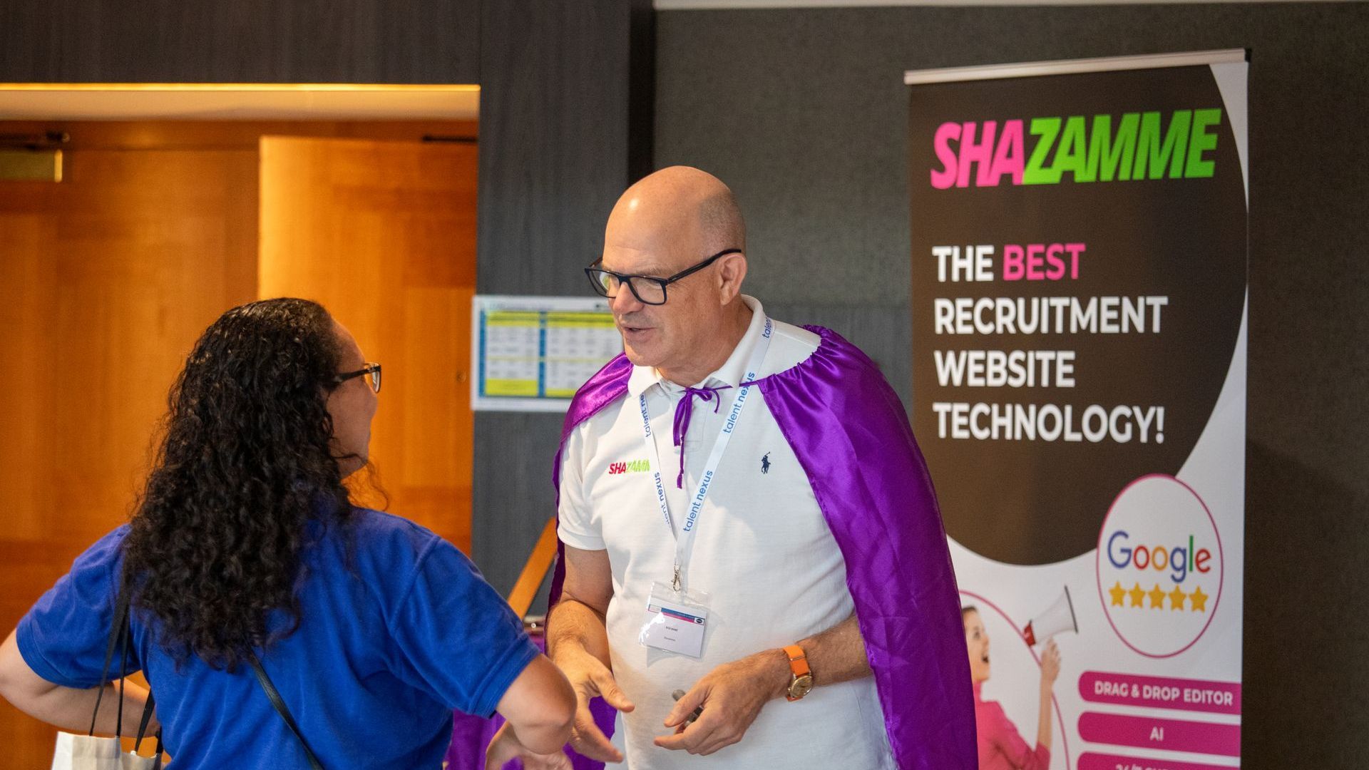 A man in a purple cape is standing next to a woman in a blue shirt.