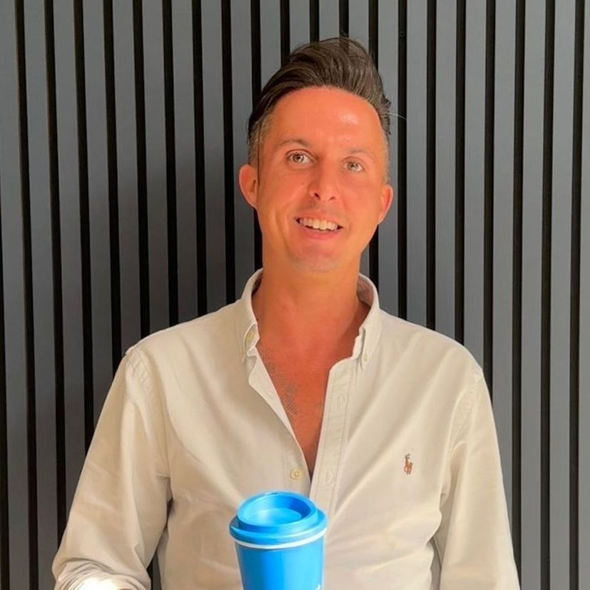A man in a grey shirt is smiling for the camera