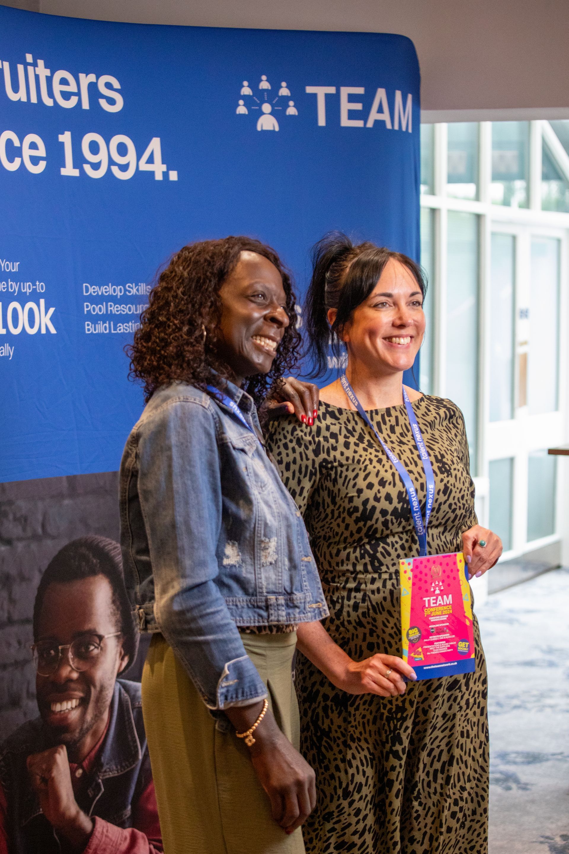 Two women are posing for a picture in front of a sign that says team