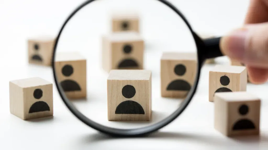 A magnifying glass is being used to look at wooden blocks with people 's faces on them.