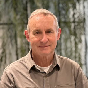 A man in a grey shirt is smiling for the camera