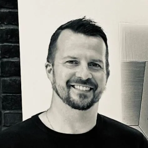 A man with a beard is smiling in a black and white photo.