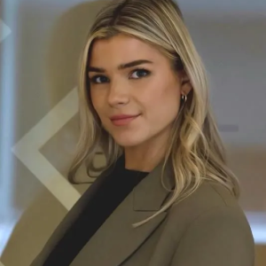 A woman wearing a blazer and earrings is looking at the camera.