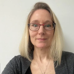 A woman wearing glasses and a necklace is smiling for the camera.