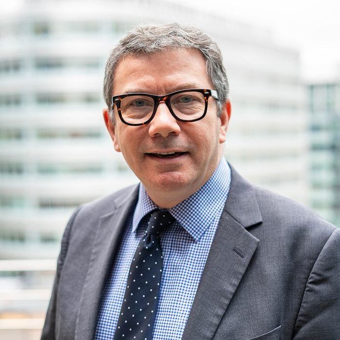 A man in a grey shirt is smiling for the camera