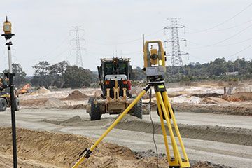 A construction site with a bulldozer and a theodolite on a tripod.