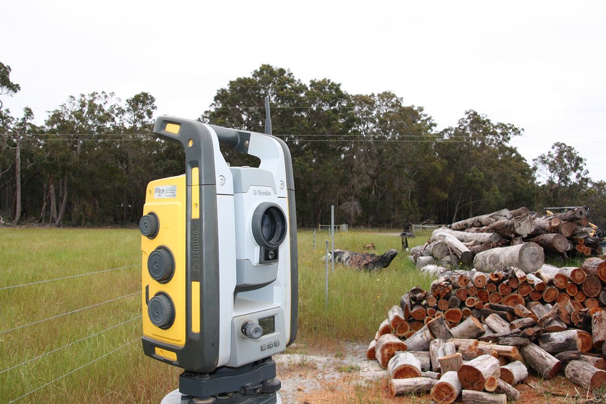 A total station is sitting in a field next to a pile of logs.